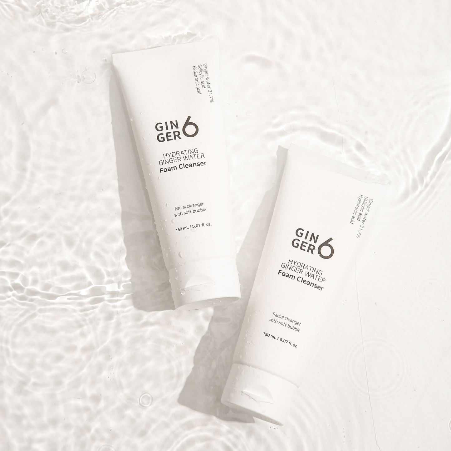 Two tubes of Ginger6 hydrating ginger water foam cleanser lying in clean, rippling water
