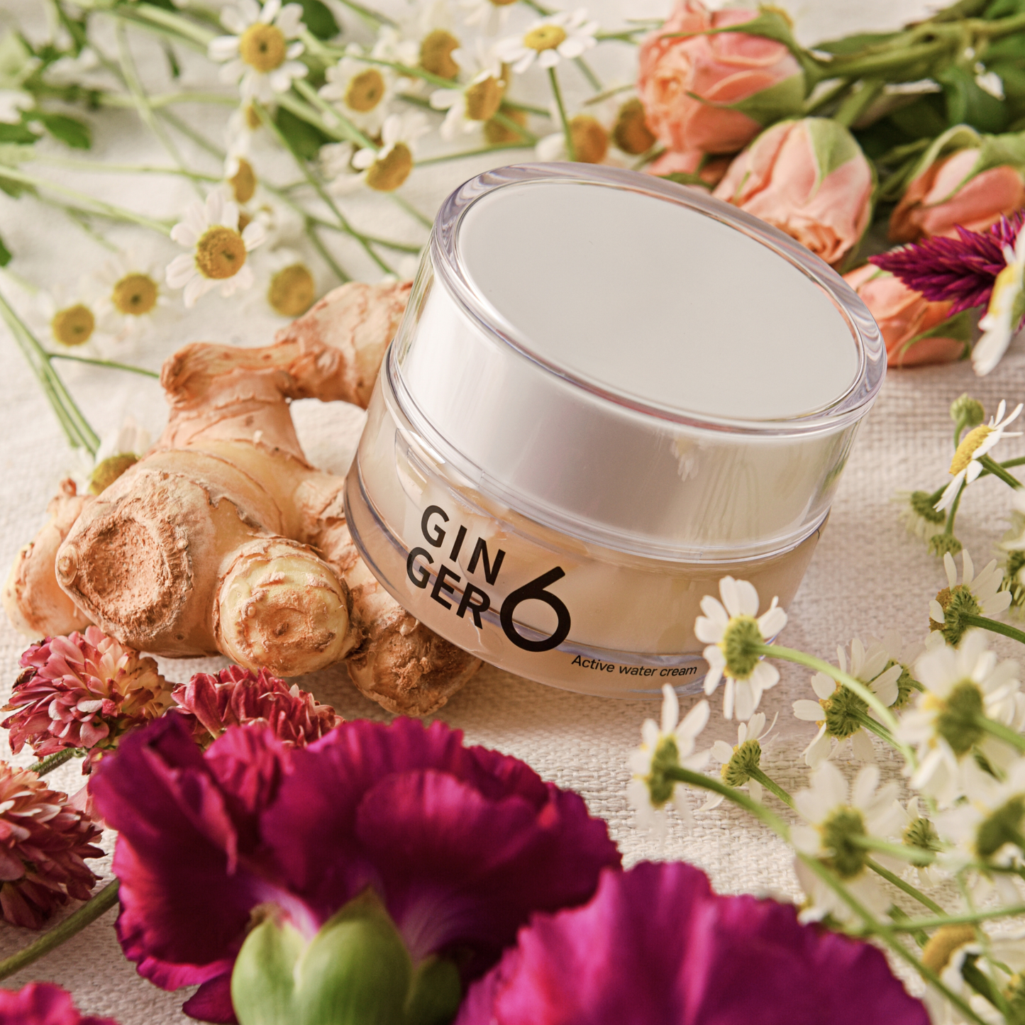 Ginger6 Active Water Day Cream surrounded by fresh flowers and raw ginger root on a textured cloth