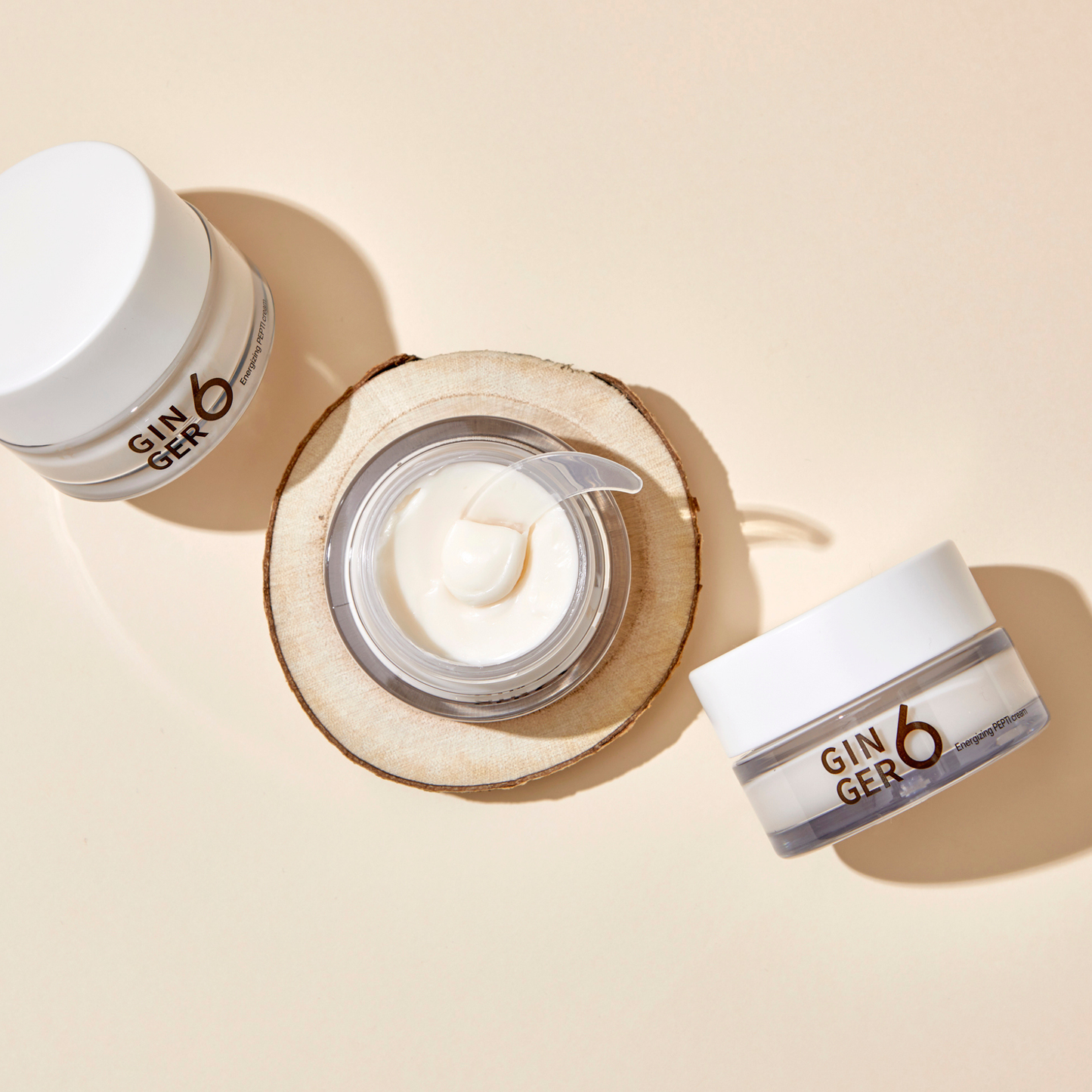 Top-down view of Ginger6 Energizing PEPTI Night Cream open jar with a spatula showing the creamy texture on a wood slice