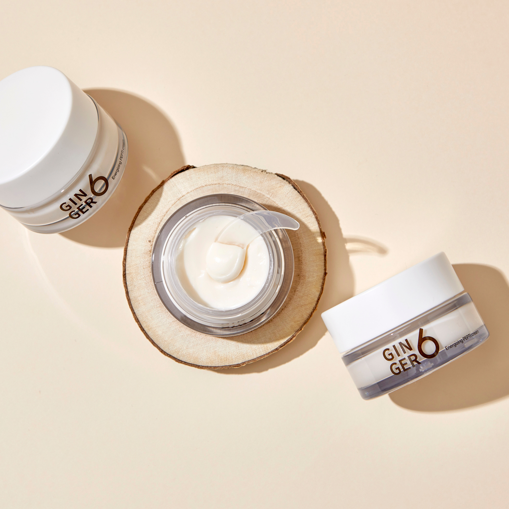 Top-down view of Ginger6 Energizing PEPTI Night Cream open jar with a spatula showing the creamy texture on a wood slice