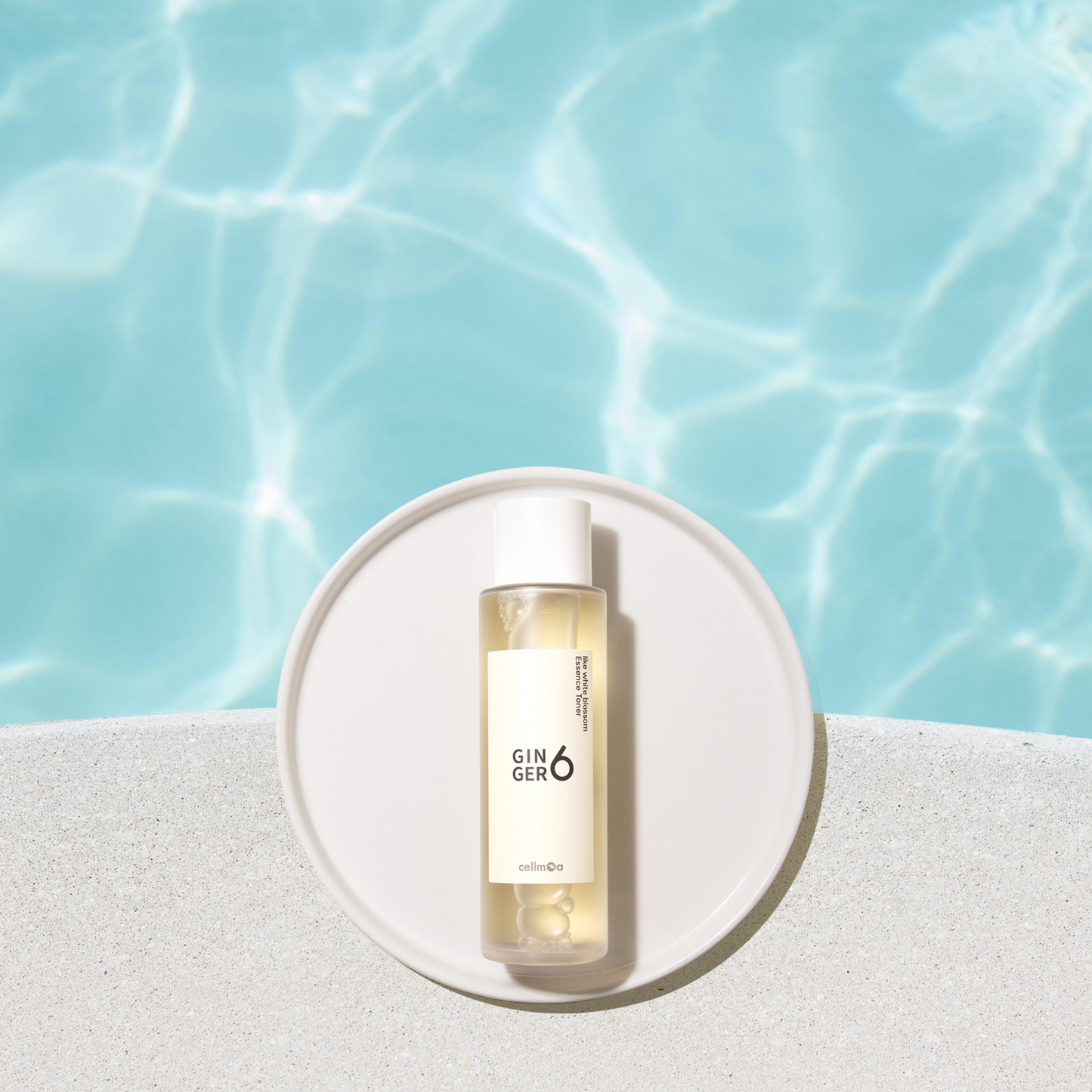 Ginger6 Like White Blossom Essence Toner placed on a white round tray over clear, rippling blue water