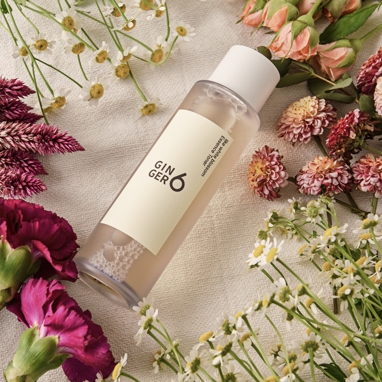 Ginger6 Like White Blossom Essence Toner surrounded by fresh pink and white flowers on a textured cloth