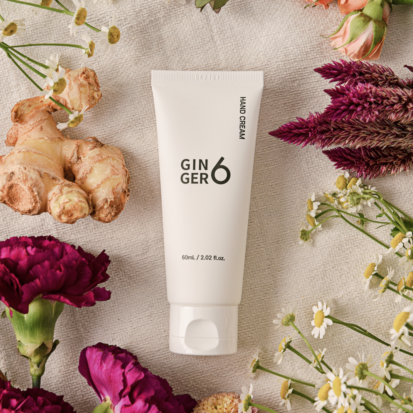Ginger6 Hand Cream surrounded by fresh flowers and raw ginger root on a textured cloth