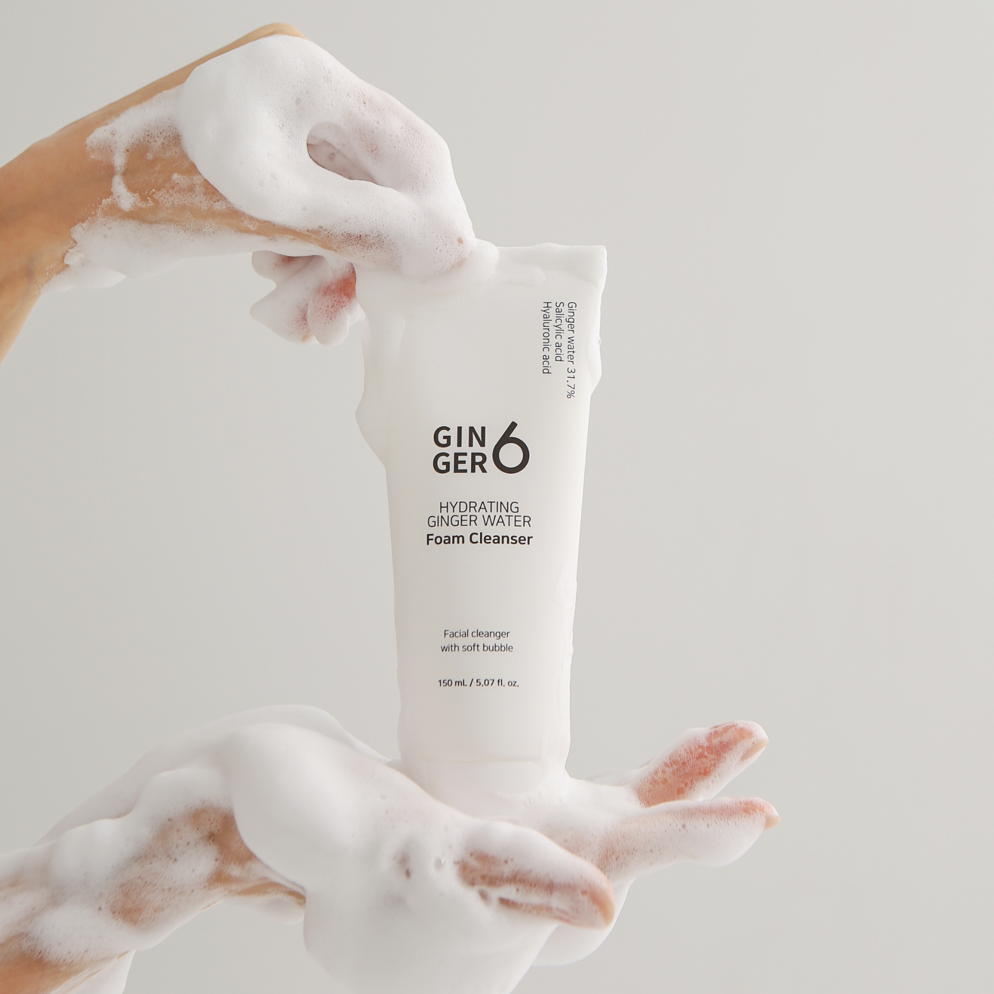 Hands holding Ginger6 hydrating ginger water foam cleanser, demonstrating its rich and soft micro-bubble lather