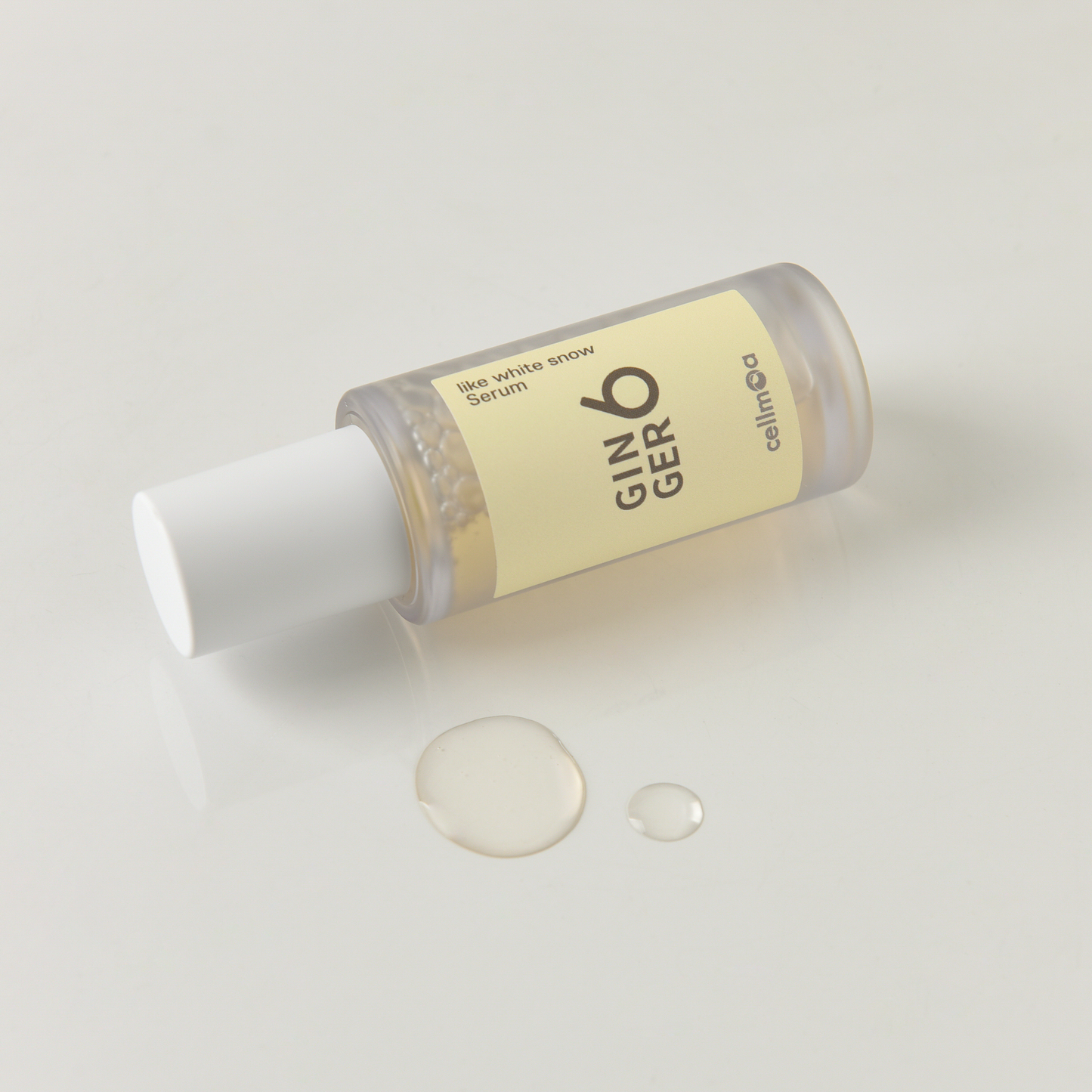 Close-up of Ginger6 Like White Snow Serum bottle dispensing clear, hydrating liquid drops on a white surface