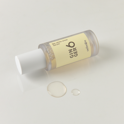Close-up of Ginger6 Like White Snow Serum bottle dispensing clear, hydrating liquid drops on a white surface