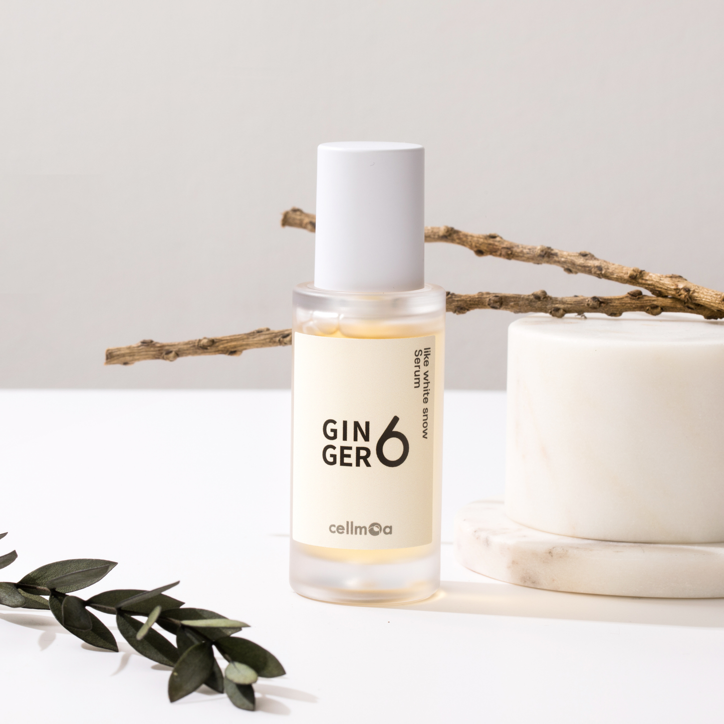Ginger6 Like White Snow Serum placed next to a white marble podium and dry natural branches on a clean surface