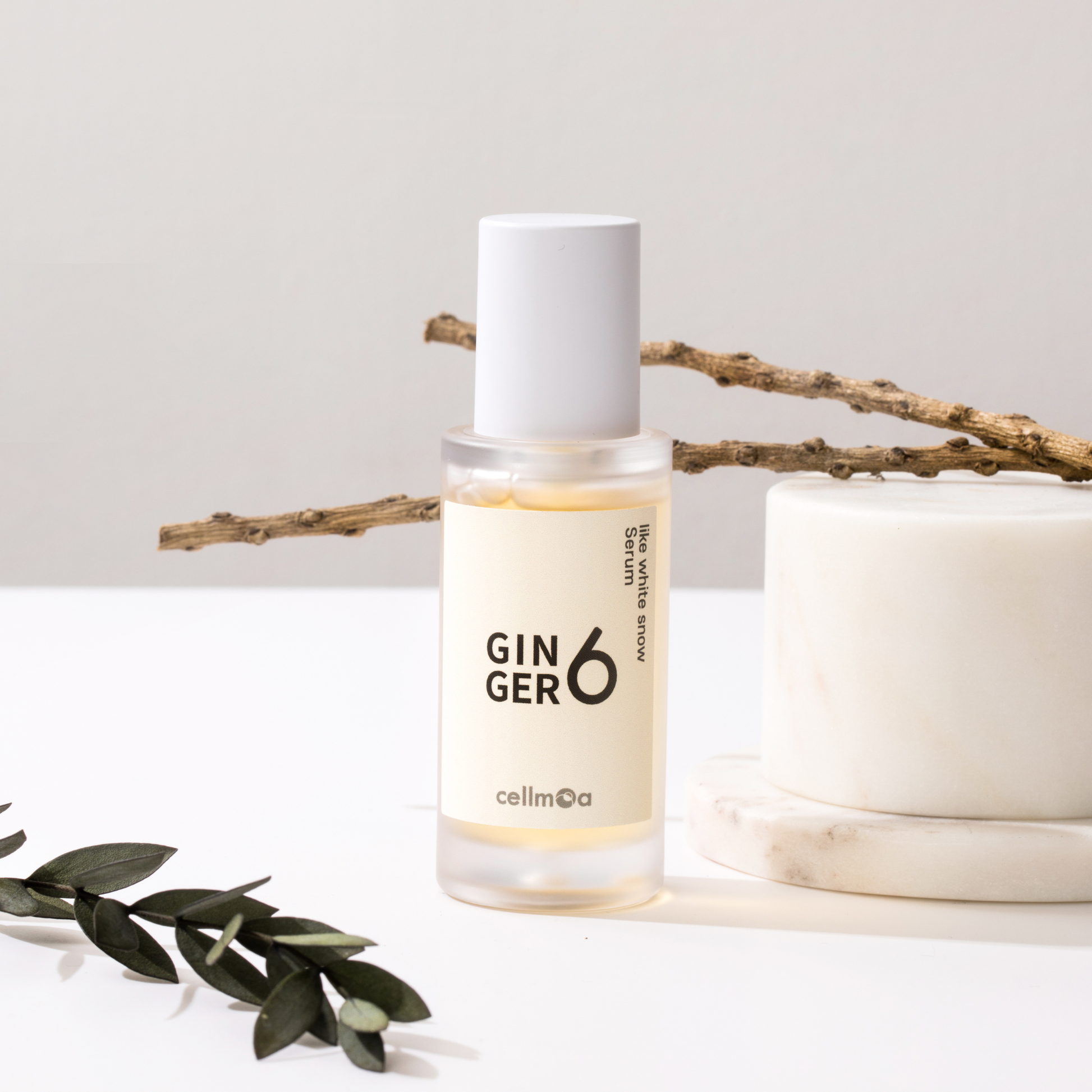 Ginger6 Like White Snow Serum placed next to a white marble podium and dry natural branches on a clean surface